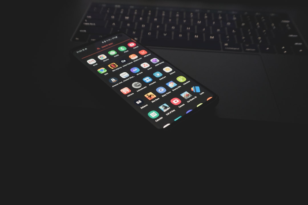 ノートパソコンのキーボードの上に置かれたアプリアイコンが並ぶスマートフォン