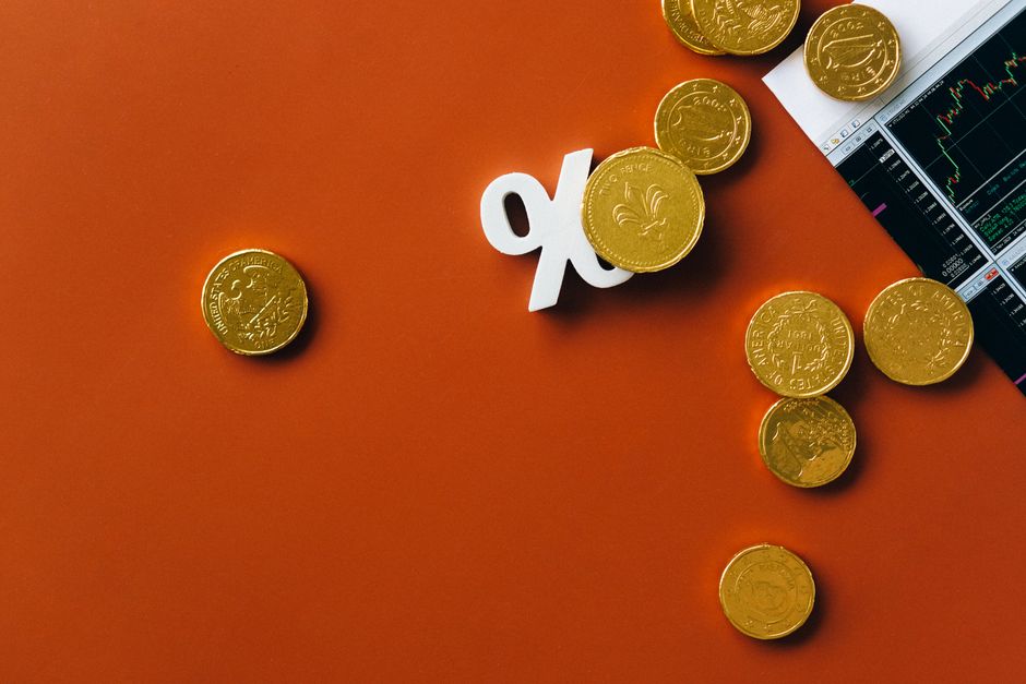 オレンジ色の背景に散らばった金色のコインとパーセント記号