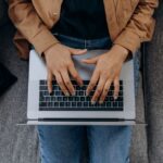 膝の上のノートパソコンでキーボードを打つ手元