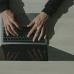 上から見たノートパソコンのキーボードを打つ両手