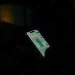 暗い部屋で片手に持ったスマートフォンに表示された値動きのチャート画面