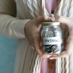 SAVINGSと書かれた小銭入りの瓶を両手で持つ人