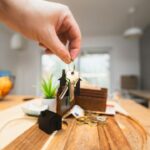 木のテーブルの上で家の鍵と小さな家の模型に手を伸ばす様子