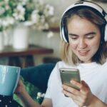 ヘッドホンをつけてソファに座りスマートフォンを操作する女性