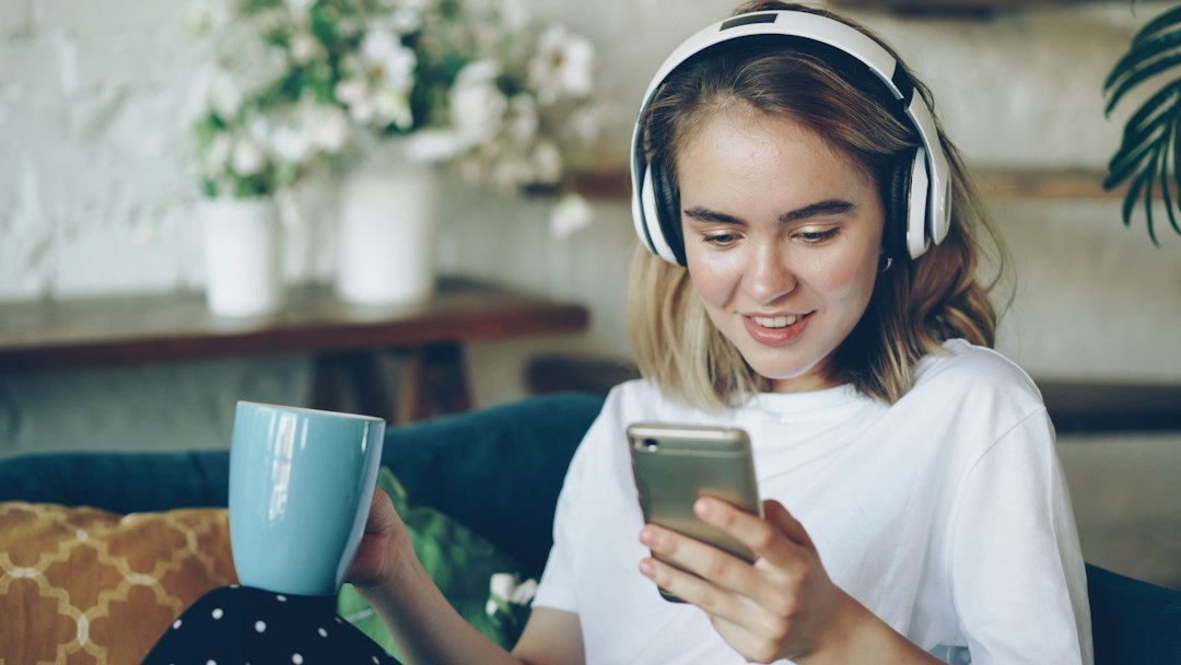 ヘッドホンをつけてソファに座りスマートフォンを操作する女性