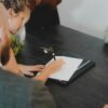 テーブルを囲んで書類にサインしながら相談している人たちの手元