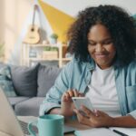 自宅のデスクでスマートフォンを見ながら微笑む女性