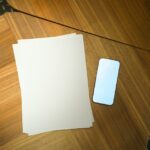 暗い木製テーブルに置かれた白紙とスマートフォン
