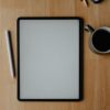 白いタブレット端末とApple Pencil、コーヒーカップが置かれた木製デスク