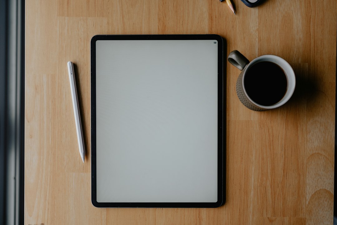 白いタブレット端末とApple Pencil、コーヒーカップが置かれた木製デスク
