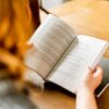 カフェでノートとペンを手にしながら本を読む女性