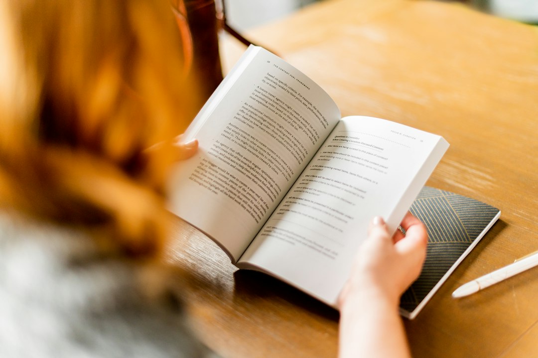 カフェでノートとペンを手にしながら本を読む女性