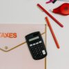 電卓と赤いペン、TAXESと書かれたピンクの書類ケース