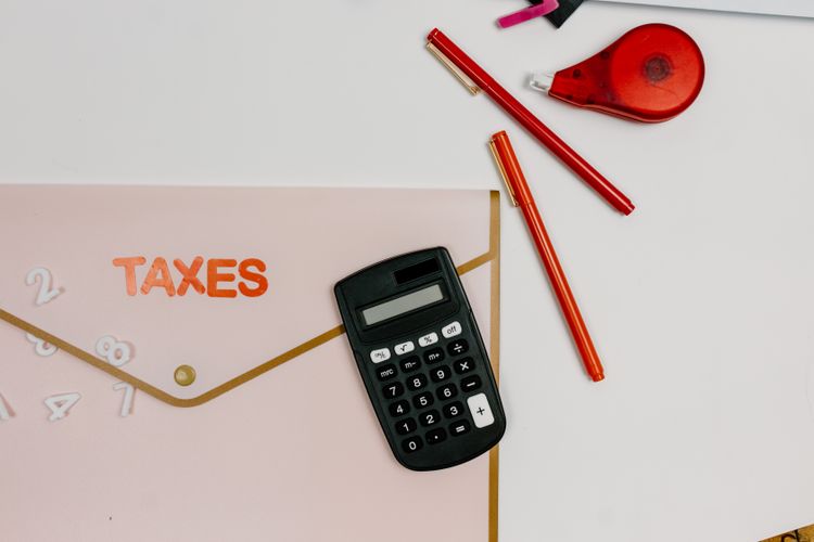 電卓と赤いペン、TAXESと書かれたピンクの書類ケース