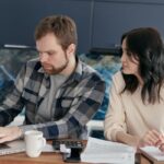 リビングのソファでノートパソコンを見ながら相談する夫婦
