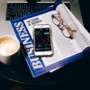 「BUSINESS」の雑誌とコーヒー、スマートフォン、眼鏡が置かれたテーブル