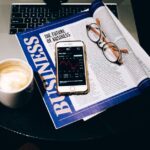 「BUSINESS」の雑誌とコーヒー、スマートフォン、眼鏡が置かれたテーブル