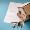青い背景に置かれた木製のミニチュアハウスと書類