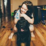 床で黒い犬を抱きしめて笑う女の子