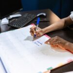 大きな卓上カレンダーにペンで予定を書き込む女性の手元