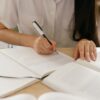 開いた本の横でノートに書き込む女性の手元