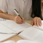 開いた本の横でノートに書き込む女性の手元