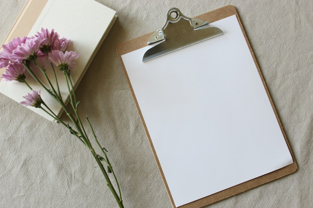 何も書かれていない白紙を挟んだクリップボードとピンクの花