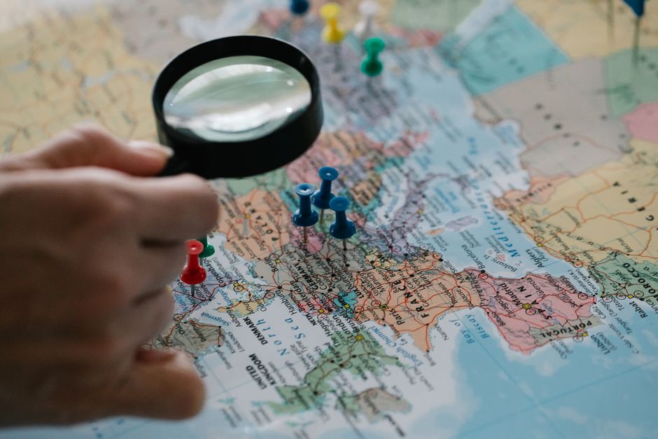 ピンが刺さった世界地図を虫眼鏡でのぞく手元