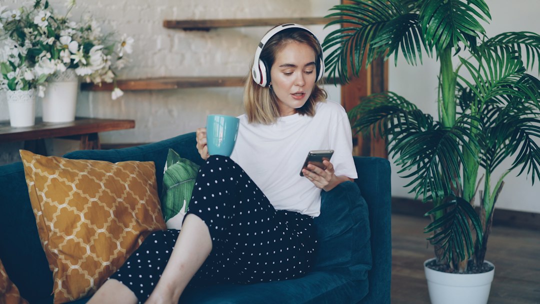 ヘッドホンをつけソファでスマートフォンを見る女性