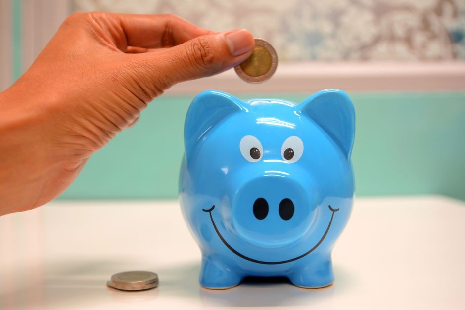 青い豚の貯金箱に硬貨を入れようとする手