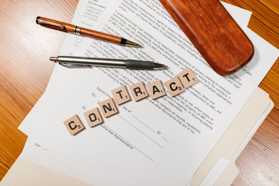 「CONTRACT」の文字タイルが置かれた契約書とペン