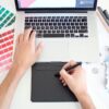 パントーンのカラーチャートとノートパソコンでデザイン作業をする手元