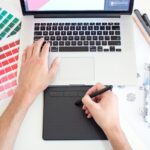 パントーンのカラーチャートとノートパソコンでデザイン作業をする手元