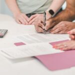 電卓のそばで書類に署名する人たちの手元
