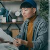 ニット帽をかぶった男性がデスクでノートパソコンに向かう様子