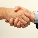 スーツの男性とチェック柄シャツの男性が握手する手元