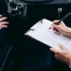 車内でクリップボードの書類にペンで記入する手元