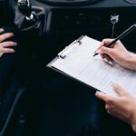 車内でクリップボードの書類にペンで記入する手元