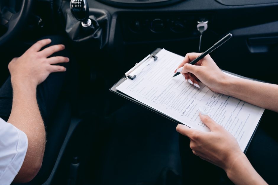 車内でクリップボードの書類にペンで記入する手元