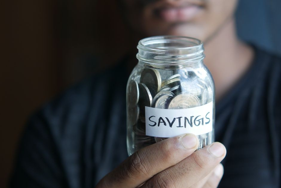 「SAVINGS」と書かれたラベル付きの貯金瓶を手に持つ人物