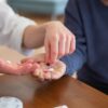 介護する人の手が高齢者の手に薬を渡している様子