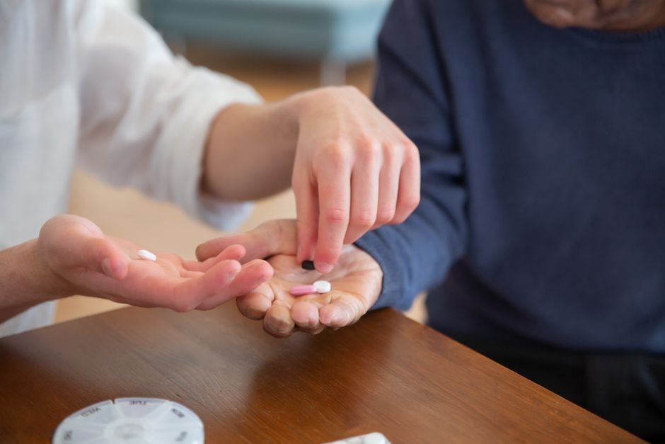 介護する人の手が高齢者の手に薬を渡している様子