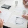 書類とコーヒーが置かれたテーブルで手を重ねて話す様子
