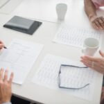 書類とコーヒーが置かれたテーブルで手を重ねて話す様子