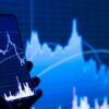 夜のリビングでスマートフォンの株価チャート画面を確認する手元