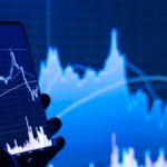 夜のリビングでスマートフォンの株価チャート画面を確認する手元