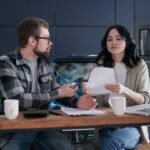 テーブルの上で複数の資料を並べて比較している夫婦の手元