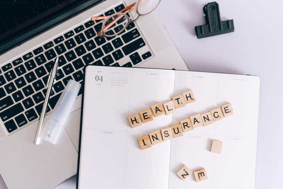 ノートパソコンと「HEALTH INSURANCE」の文字タイルを並べた手帳