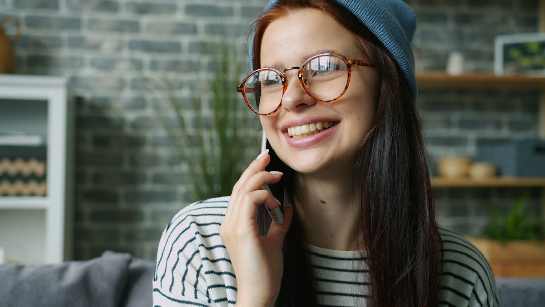 自宅のソファでスマートフォン片手に笑顔で電話をする女性