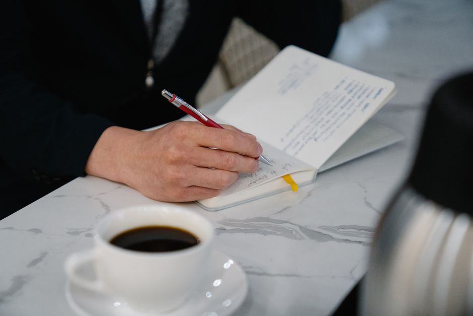 コーヒーを置いて書類に書き込む手元